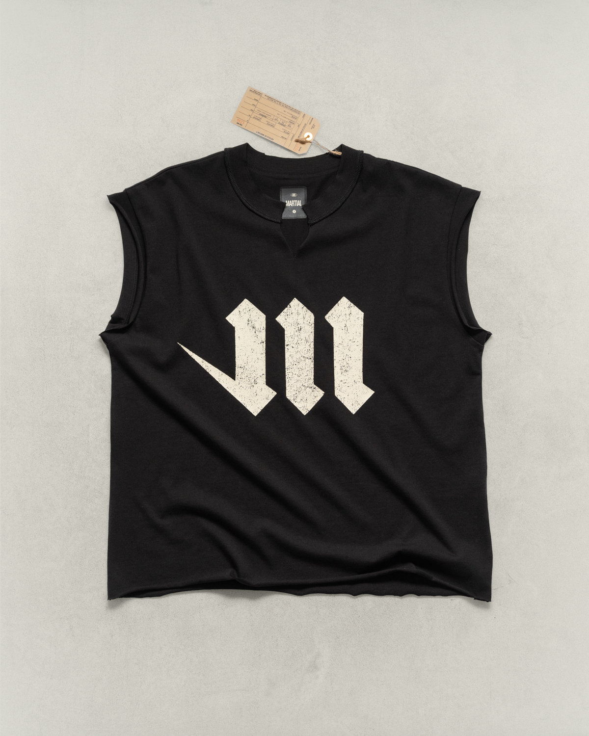 Black sleeveless shirt with a large cream-colored letter 'M' laying on a light gray background