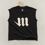 Black sleeveless shirt with a large cream-colored letter 'M' laying on a light gray background