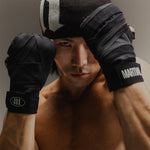 Man wearing boxing hand wraps holding his hands up in a guarded position on a gray backdrop