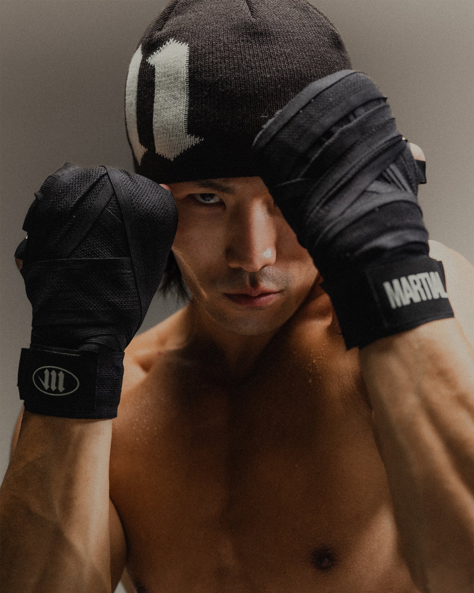 Man wearing boxing hand wraps holding his hands up in a guarded position on a gray backdrop