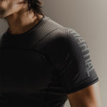 Up-close detail of black Martial rashguard on a man, standing in front of a gray background.