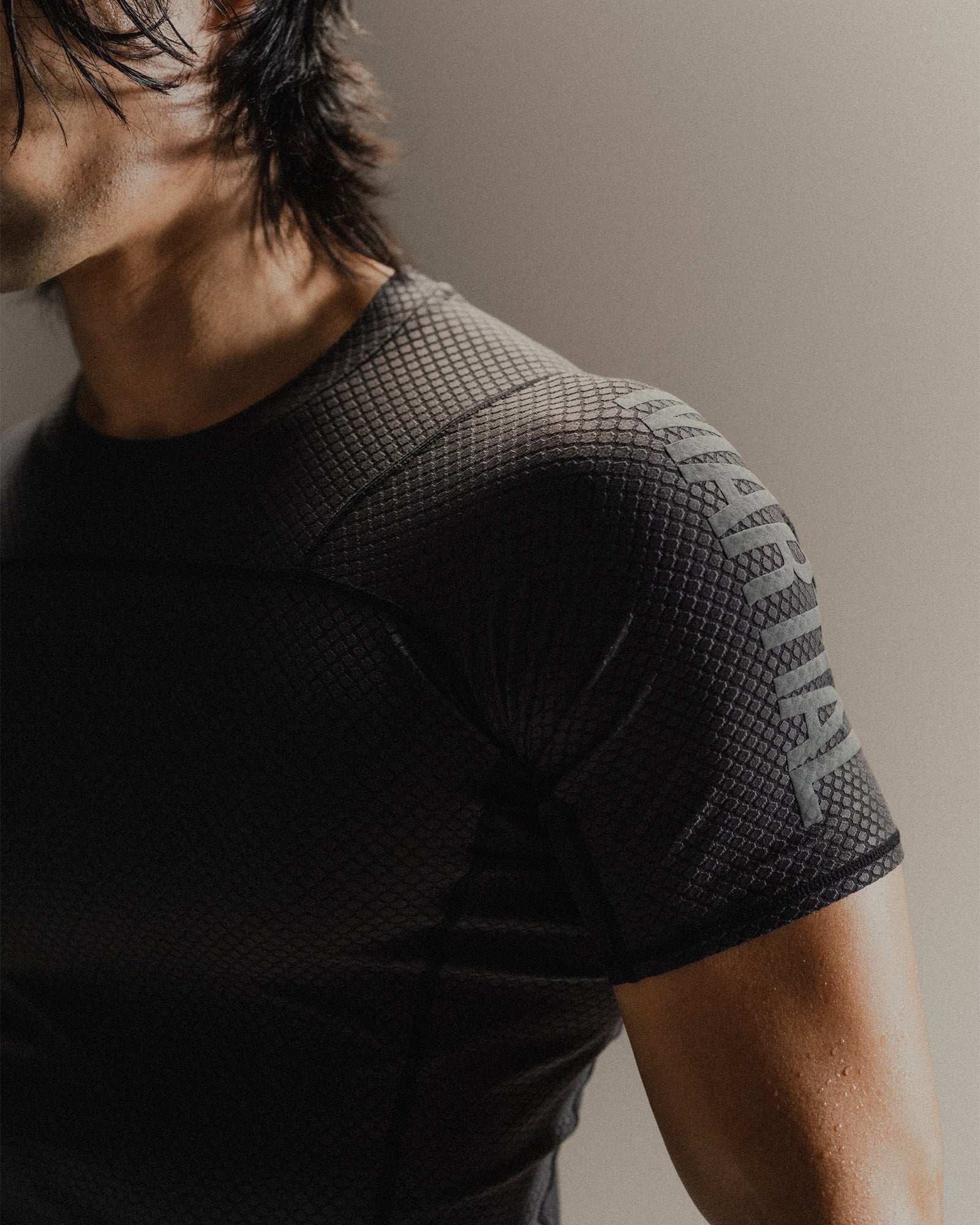 Up-close detail of black Martial rashguard on a man, standing in front of a gray background.