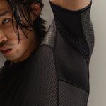 Up-close detail of man wearing Black martial rashguard, stretching to show underarm ventilation on a neutral backdrop.