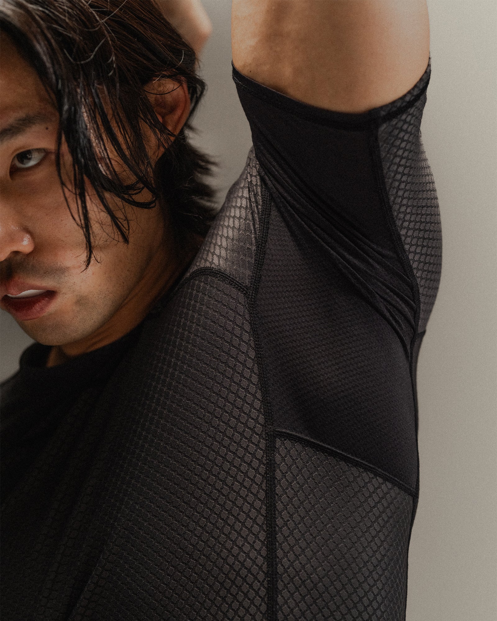 Up-close detail of man wearing Black martial rashguard, stretching to show underarm ventilation on a neutral backdrop.