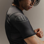 Up-close detail of black Martial rashguard on a man, standing in front of a gray background.