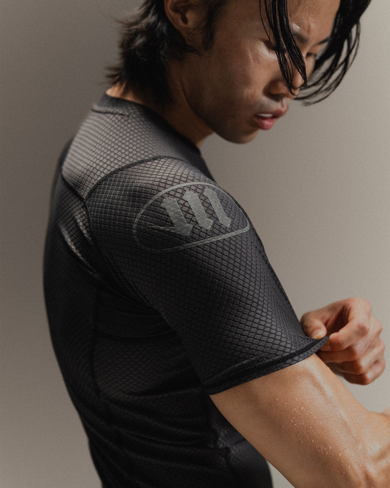 Up-close detail of black Martial rashguard on a man, standing in front of a gray background.