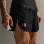 Up-close image of black Martial fight shorts with gold logo accents on a neutral backdrop.