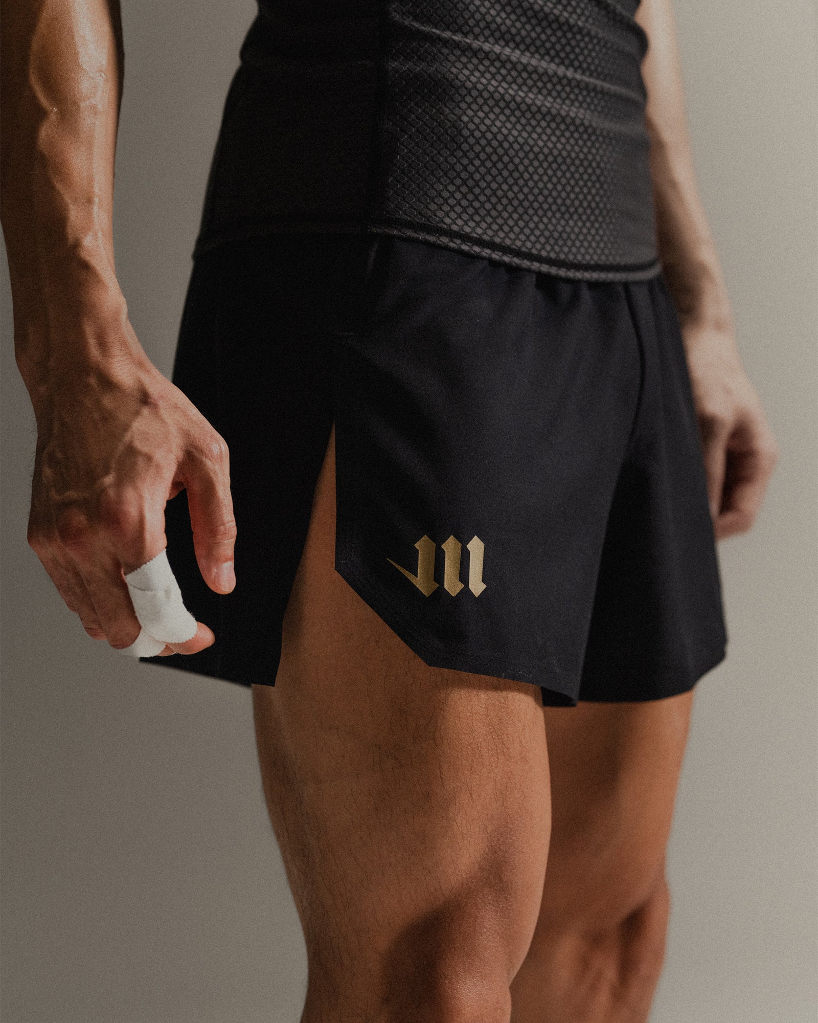Up-close image of black Martial fight shorts with gold logo accents on a neutral backdrop.