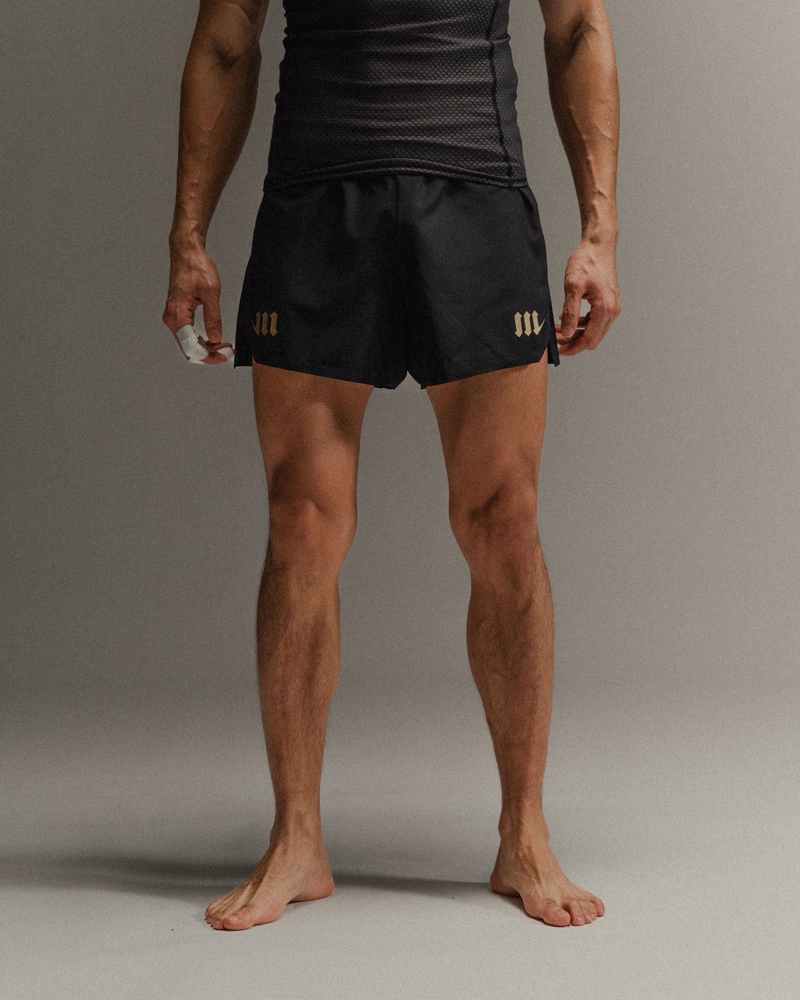 Man wearing black Martial fight shorts with gold accents on a neutral background