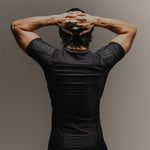 Man wearing black fight shorts and black Martial rashguard on a gray background, standing to the back to show the shoulder branding.