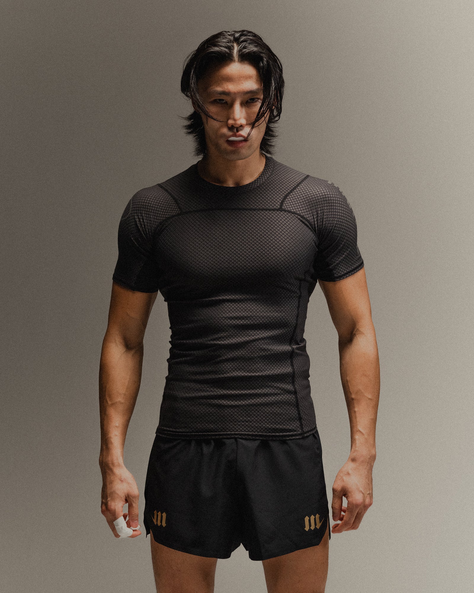 Man wearing black fight shorts and black Martial rashguard on a gray background