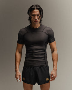 Man wearing black fight shorts and black Martial rashguard on a gray background
