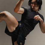 Man in black Martial rashguard and fight shorts performing a high kick on a neutral background.