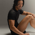 Man wearing black fight shorts and black Martial rashguard sitting on a gray background