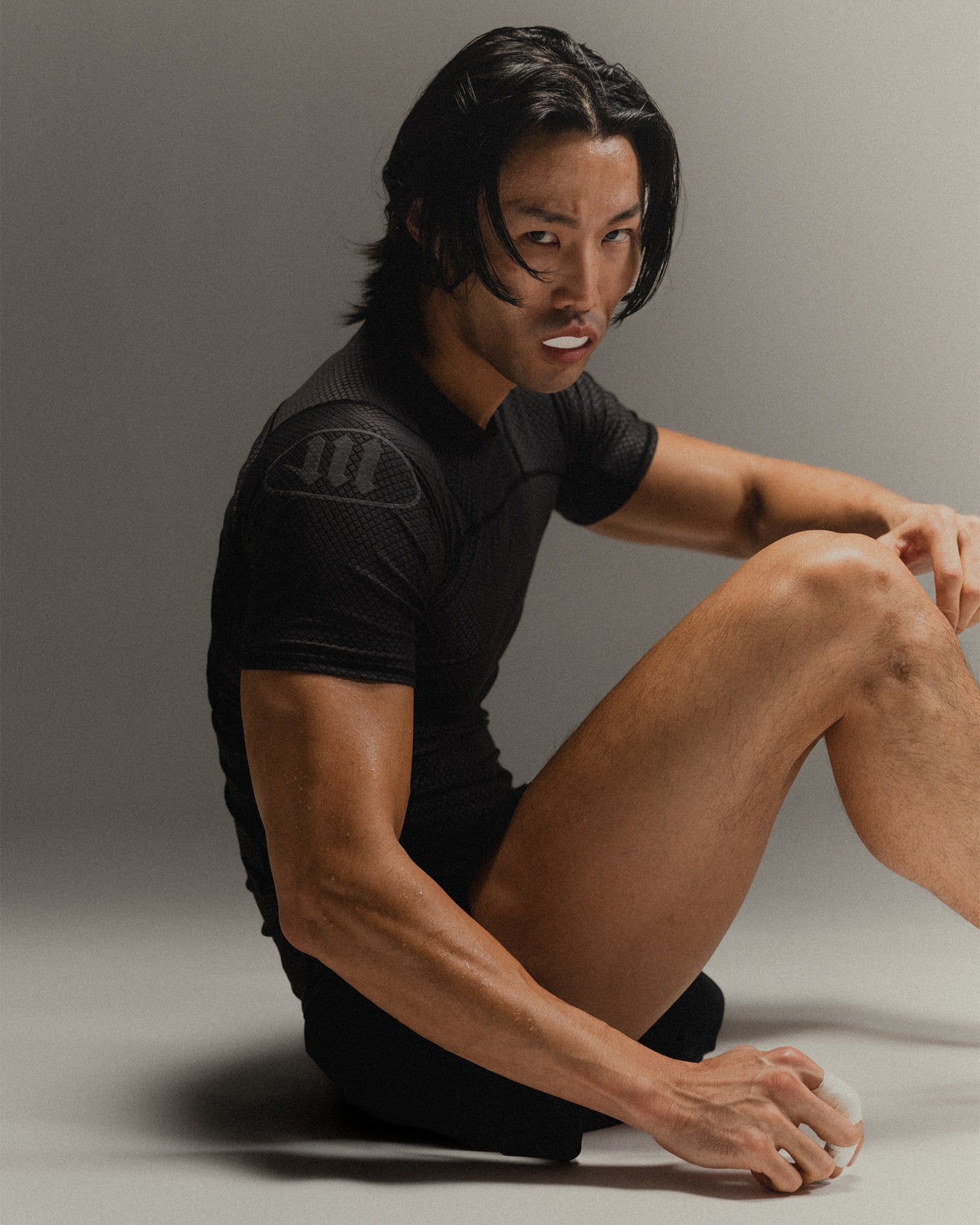Man wearing black fight shorts and black Martial rashguard sitting on a gray background