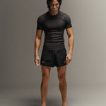 Man wearing black fight shorts and black Martial rashguard on a gray background