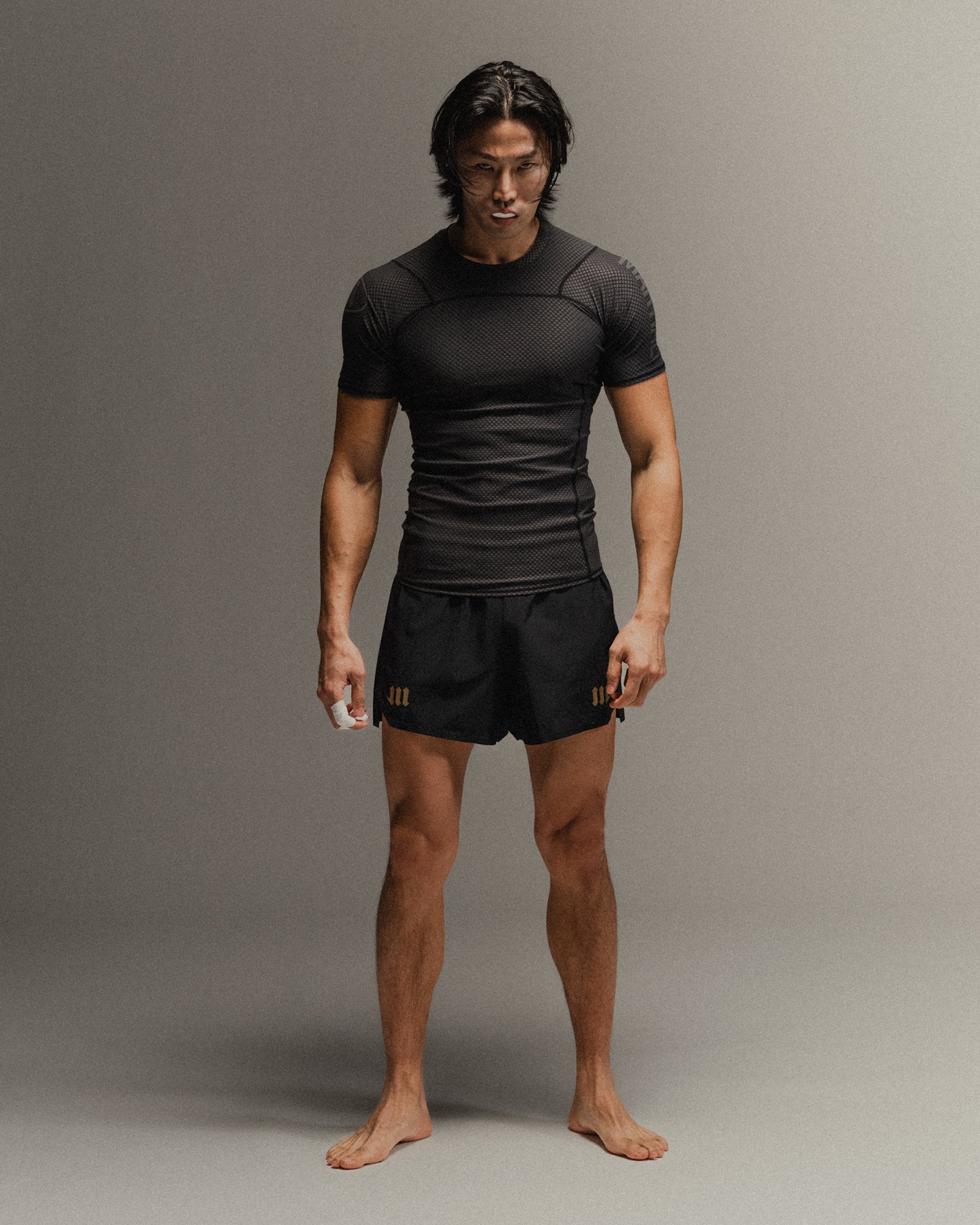 Man wearing black fight shorts and black Martial rashguard on a gray background