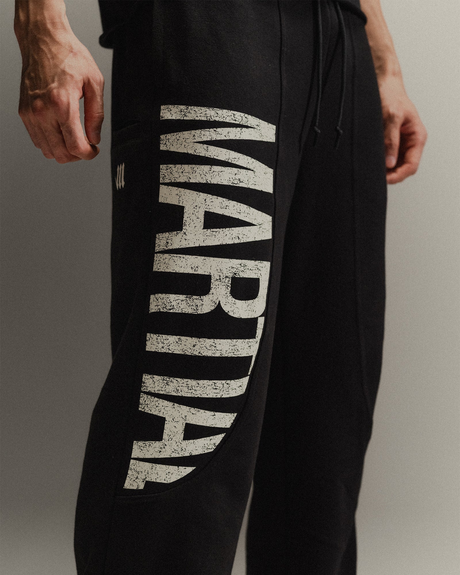 Up-close of black straight-leg sweat pants with 'Marital' graphic on a gray background