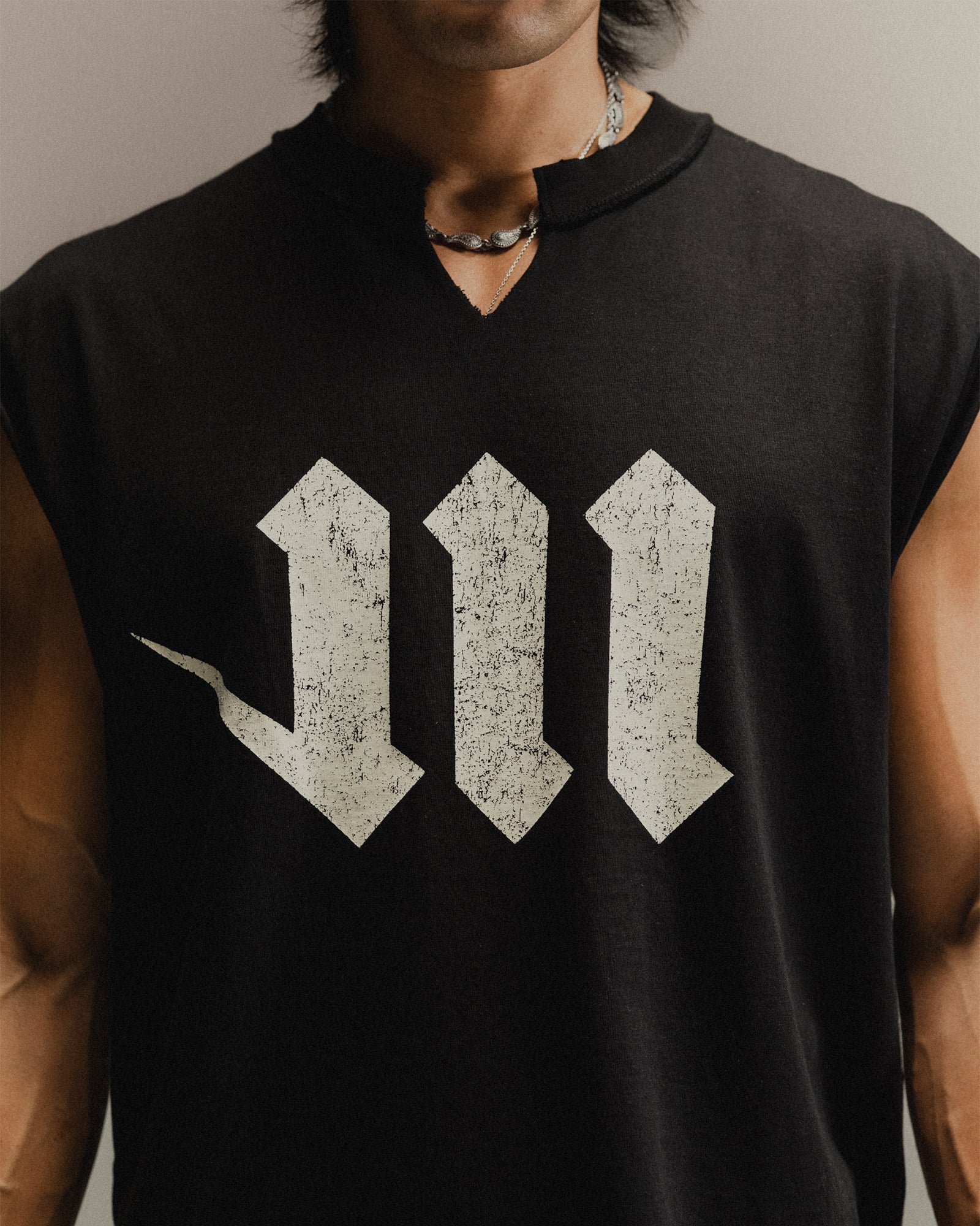 Man wearing a black sleeveless shirt with a white M logo on a neutral background