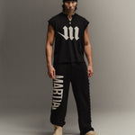 Man wearing a black sleeveless shirt with a white 'M' logo and black pants with 'Martial' printed on them, standing against a gray background.