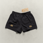 Black Martial fight shorts with gold logos  laying on a neutral backdrop.