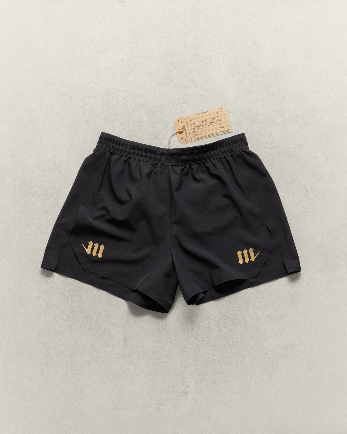 Black Martial fight shorts with gold logos  laying on a neutral backdrop.