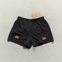 Black Martial fight shorts with gold logos  laying on a neutral backdrop.