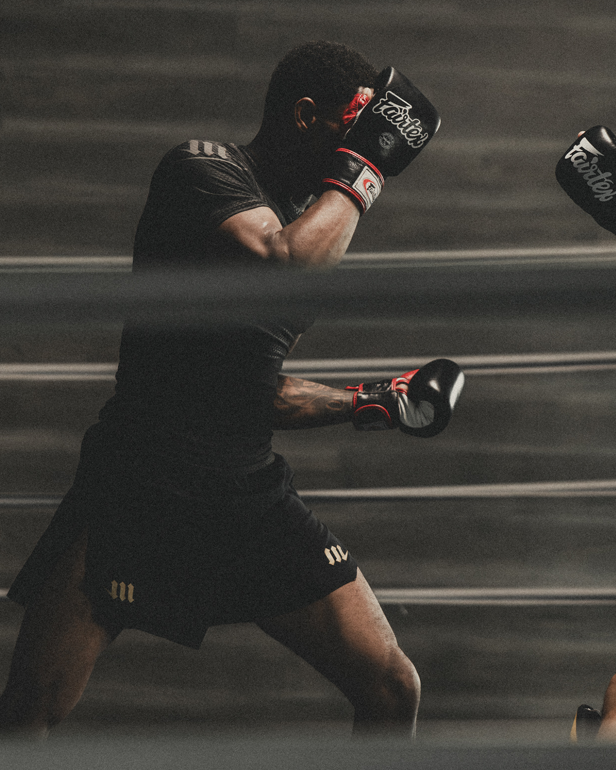 Man sparring in a boxing ring wearing black rash guard and black fight shorts.