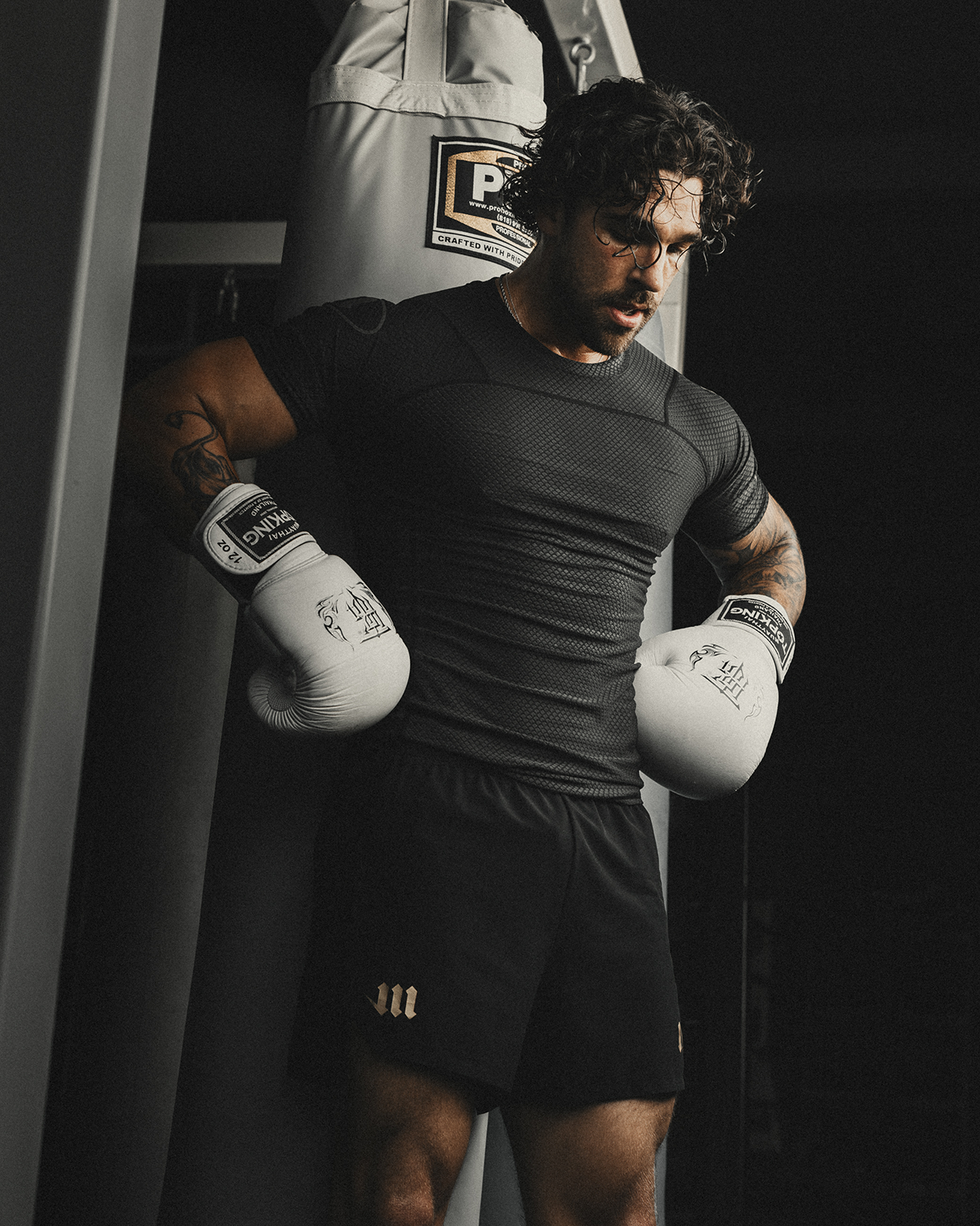 Man resting in boxing gym wearing black rash guard and black fight shorts.
