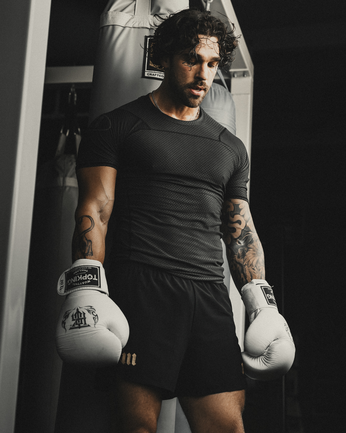 Man resting in boxing gym wearing black rash guard and black fight shorts.