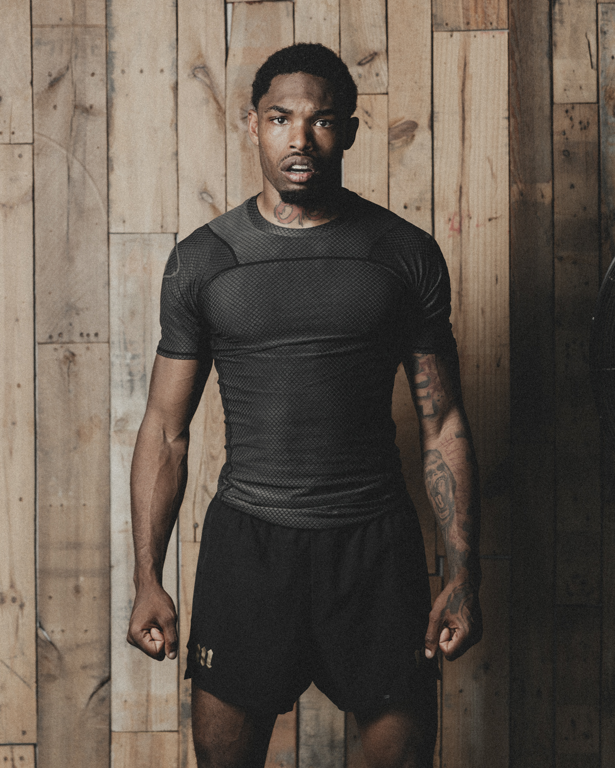 Man standing in front of wood backdrop wearing black rash guard and black fight shorts.
