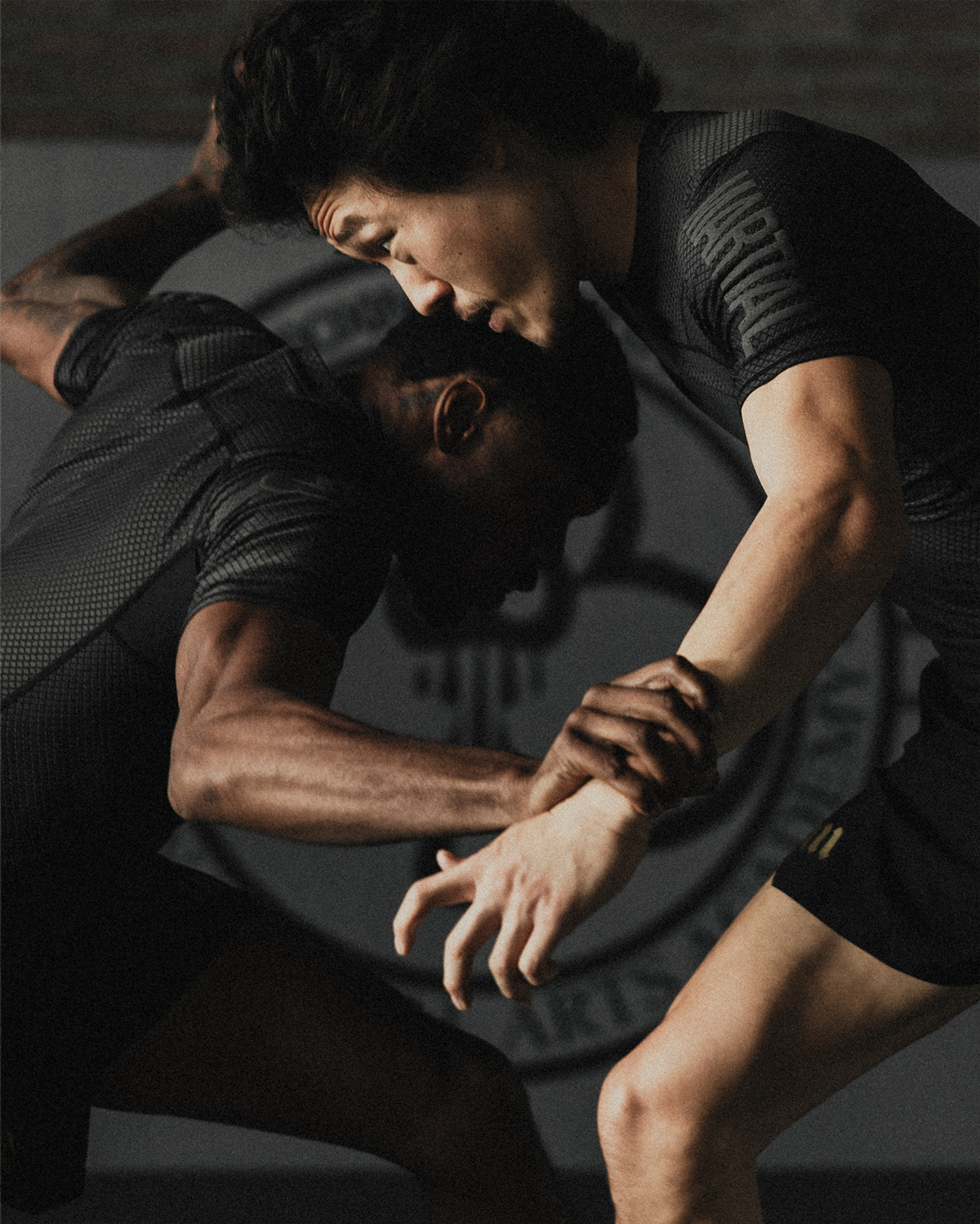 Two men grappling in black rash guards and black fight shorts.